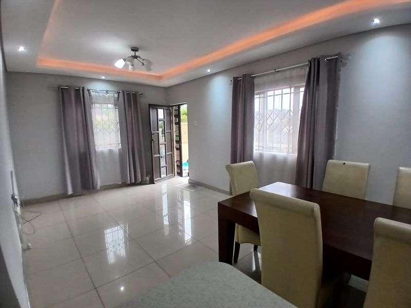 A bright open-plan living and dining area featuring polished tiled flooring, modern recessed ceiling lighting with cove accents, and secure window treatments.