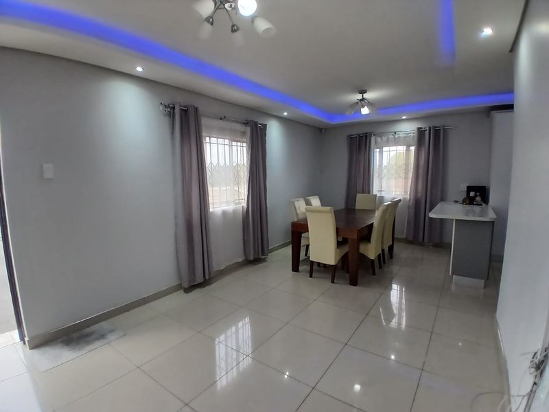 Open plan living and dining area featuring polished porcelain floor tiles, modern recessed ceiling lighting with blue LED accents, and a breakfast counter.
