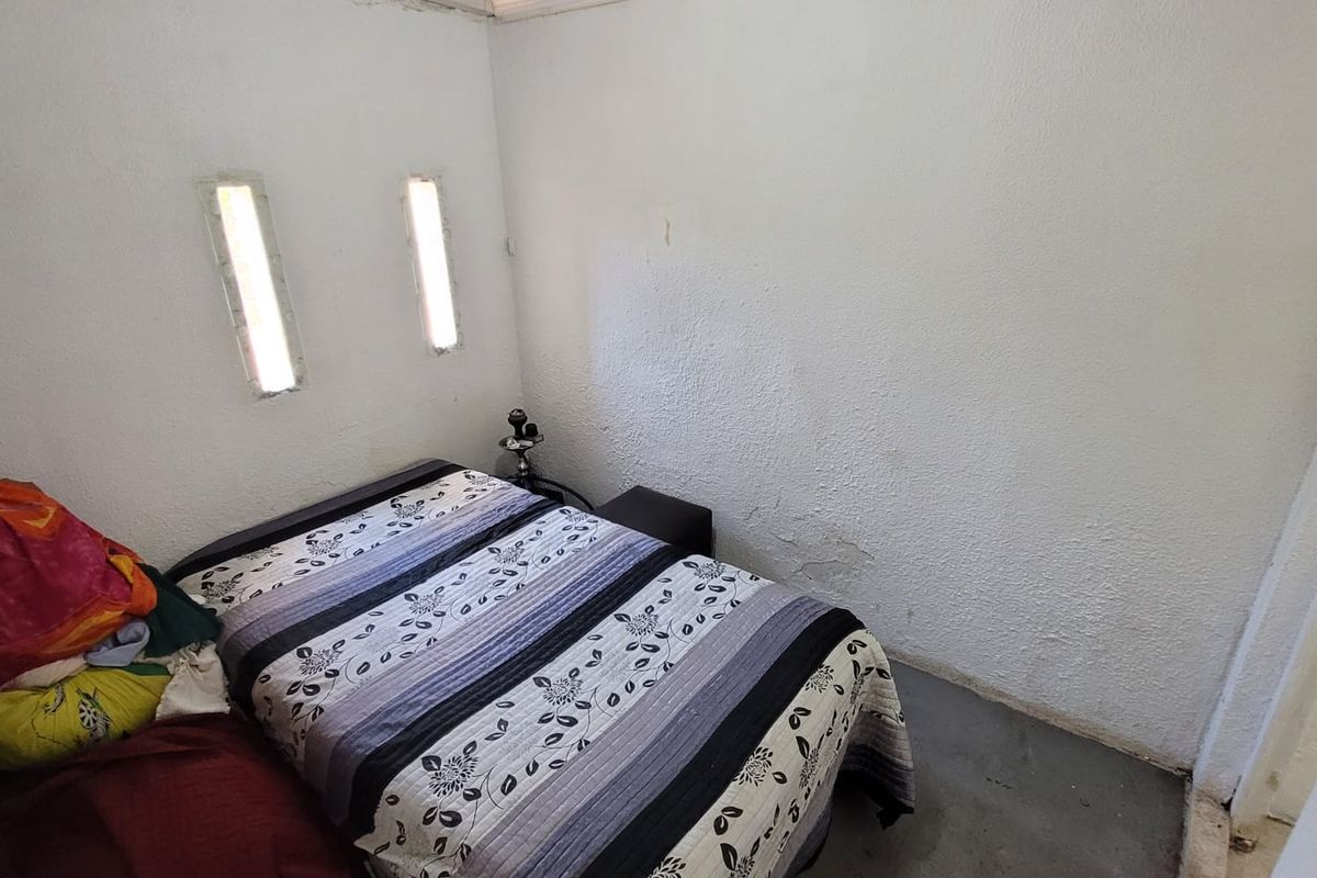 A compact bedroom featuring exposed corrugated roofing, textured walls, and vertical slit windows, requiring cosmetic updates to improve the overall finish.