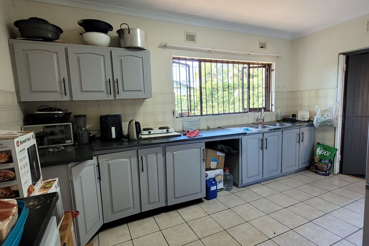 A functional kitchen featuring grey built-in cabinetry, tiled flooring, a double sink, and a window with security bars.