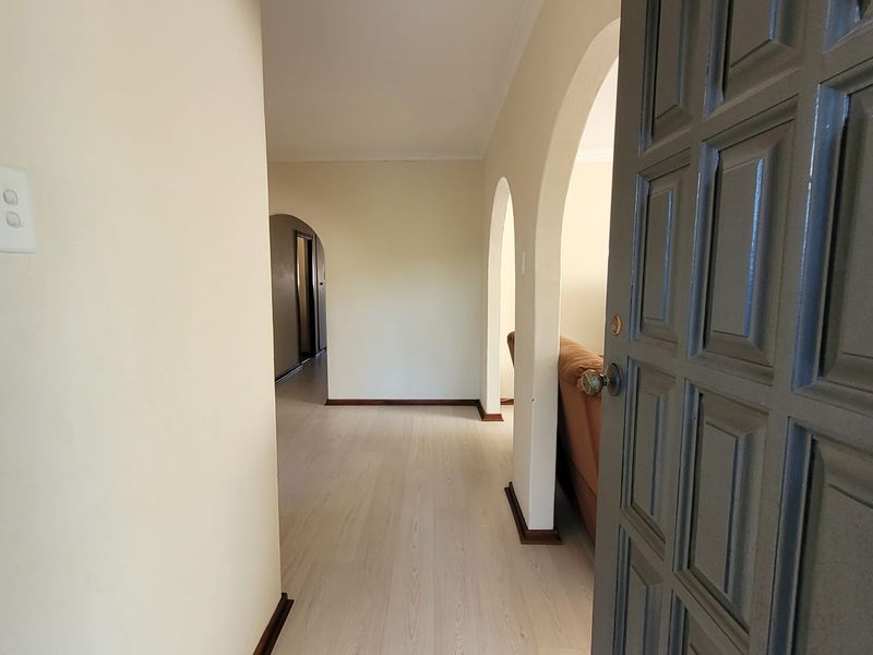 A bright hallway featuring light-toned laminate flooring and distinctive arched architectural details connecting to adjacent living spaces.