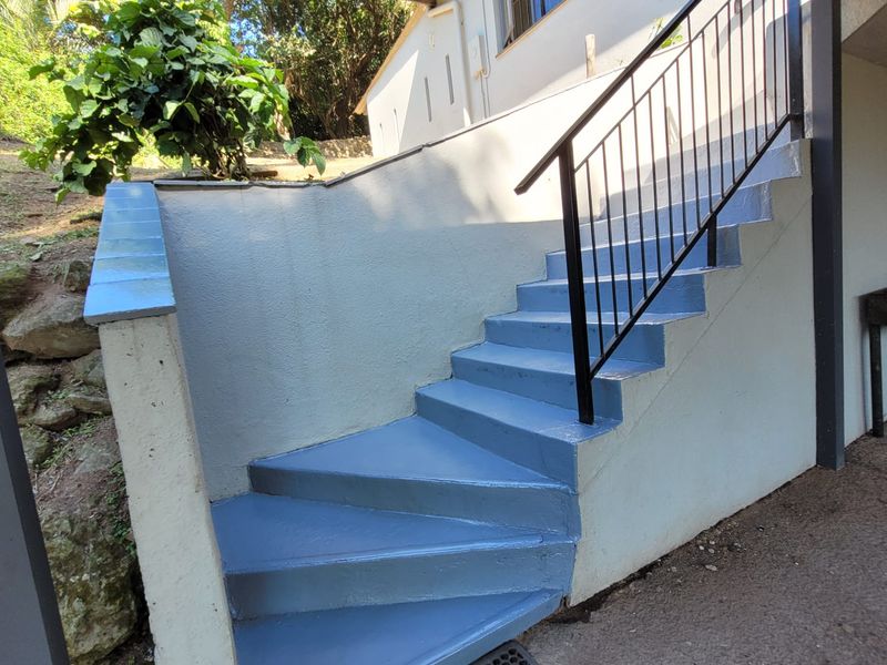 Exterior view of a painted concrete staircase with a metal handrail leading to the upper level of the property.