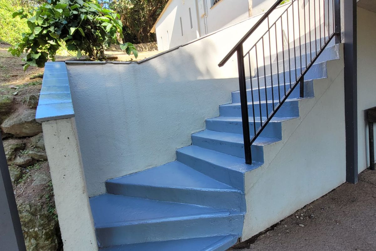 Exterior view of a painted concrete staircase with a metal handrail leading to the upper level of the property.