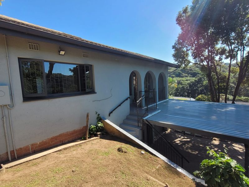 Rear exterior view of the house featuring a metal roof carport, arched veranda, and concrete staircase leading to the entrance.