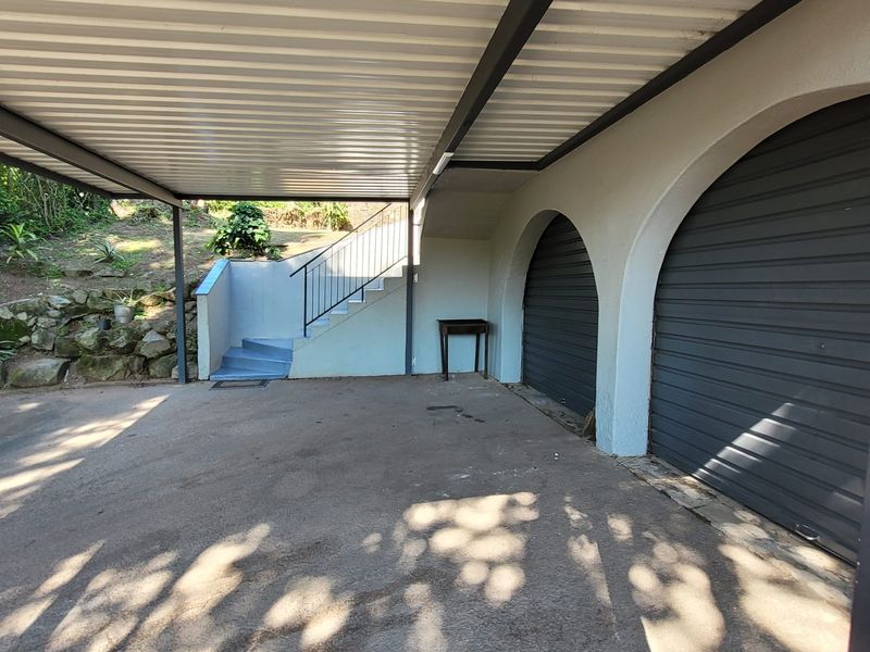 A covered double carport area featuring a concrete driveway, arched garage entrances, and an external staircase leading to the upper level.