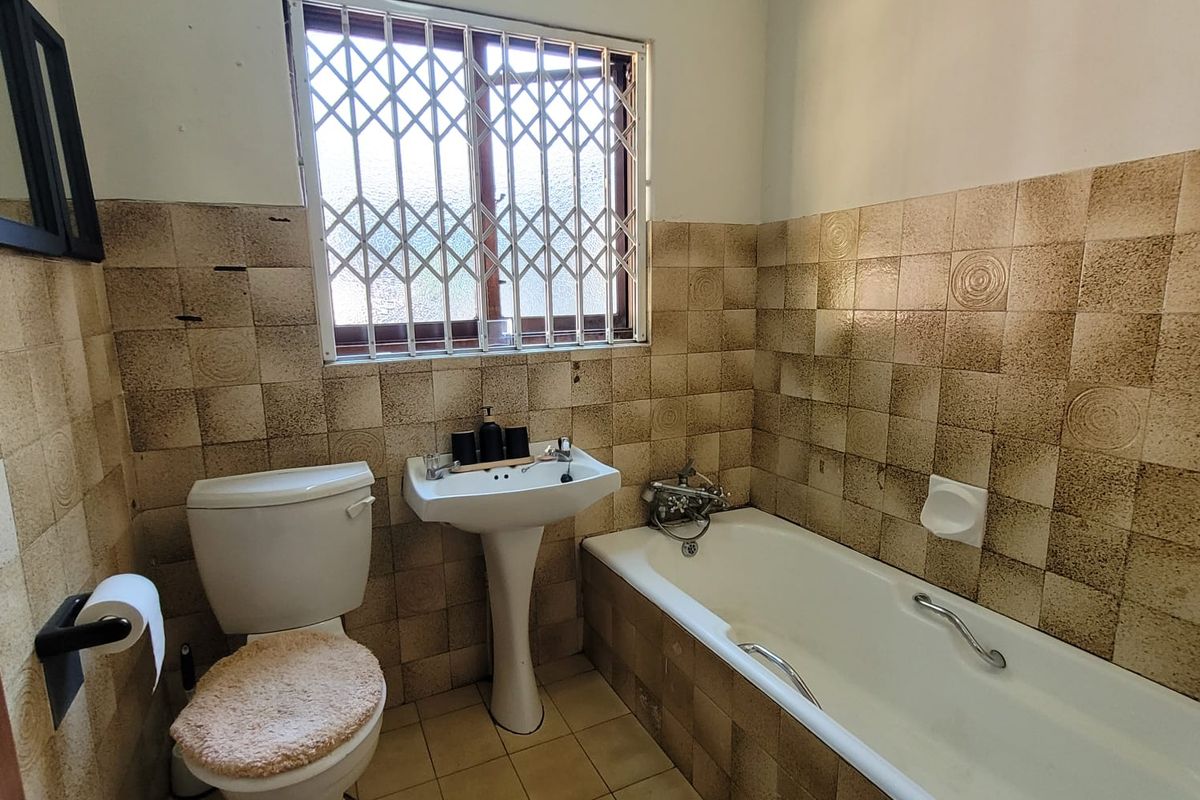 A dated bathroom featuring a pedestal basin, bathtub, and toilet, with original wall and floor tiling and a security-fitted window.