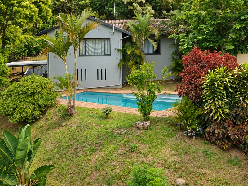A view of the rear exterior featuring a swimming pool with brick coping, set within a lush, sloped garden area.