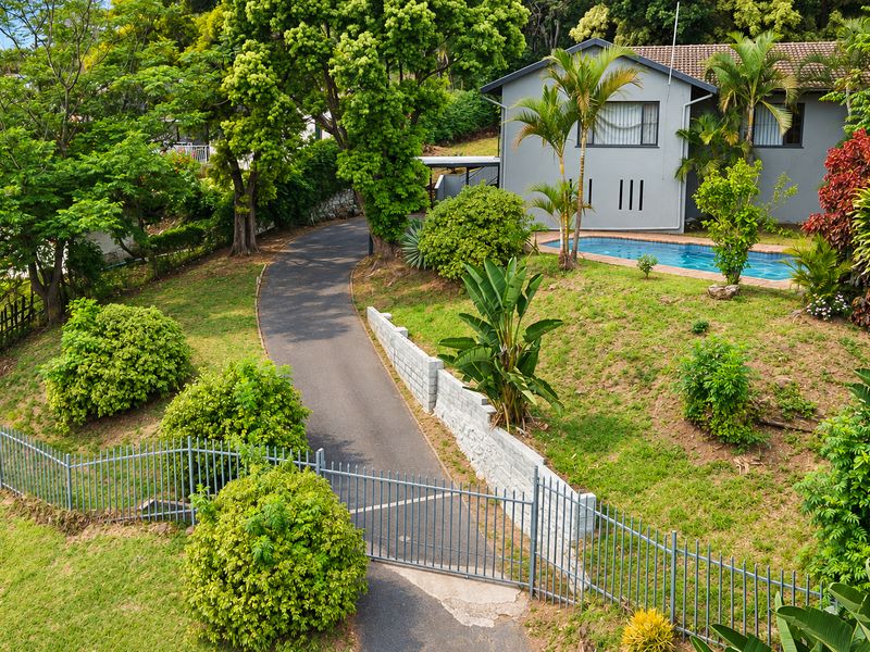 Aerial view of the property featuring a swimming pool, paved driveway, landscaped garden, and secure perimeter fencing.