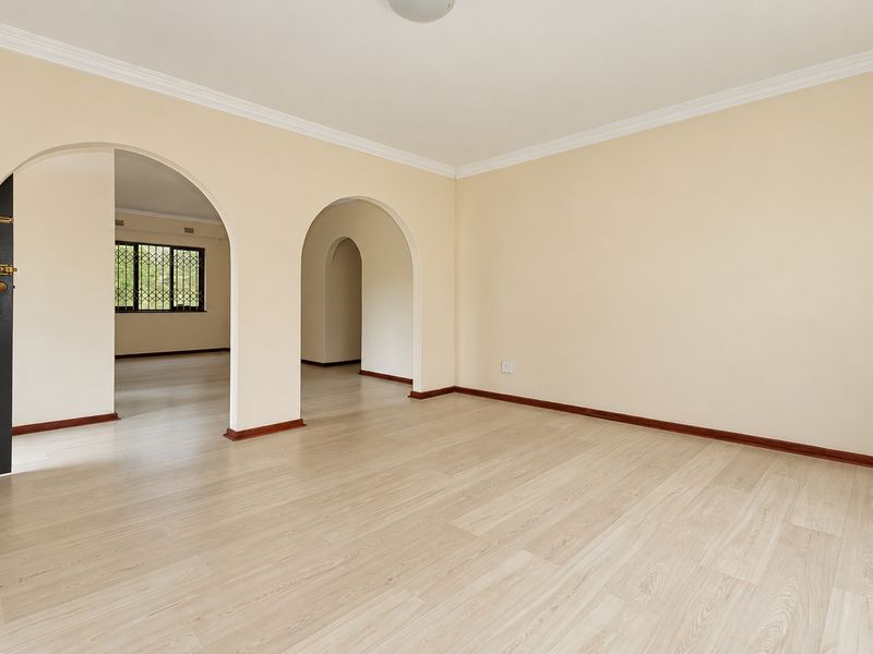 A bright, empty living area featuring arched doorways, light-toned laminate flooring, and classic cornicing, offering a versatile space for interior design.