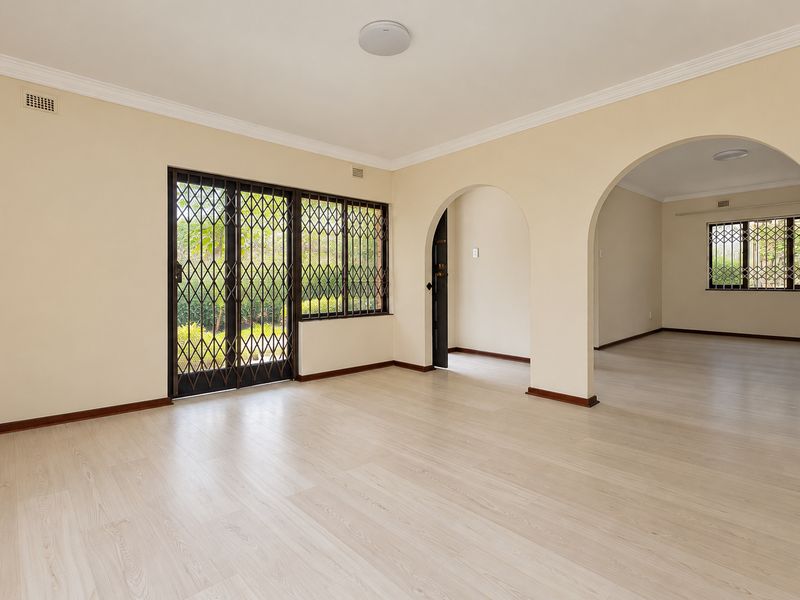 A bright and spacious living area featuring light-toned laminate flooring, elegant archways, and secure metal security gates leading to the exterior.