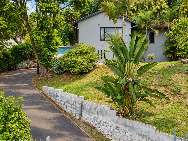 A view of the property exterior featuring a paved driveway, a concrete block retaining wall, and a glimpse of the swimming pool area.