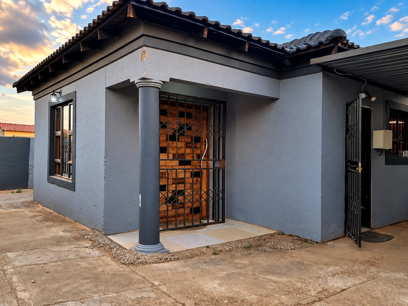 Front exterior view of a grey painted house featuring a tiled roof, security gate, and a covered carport area.