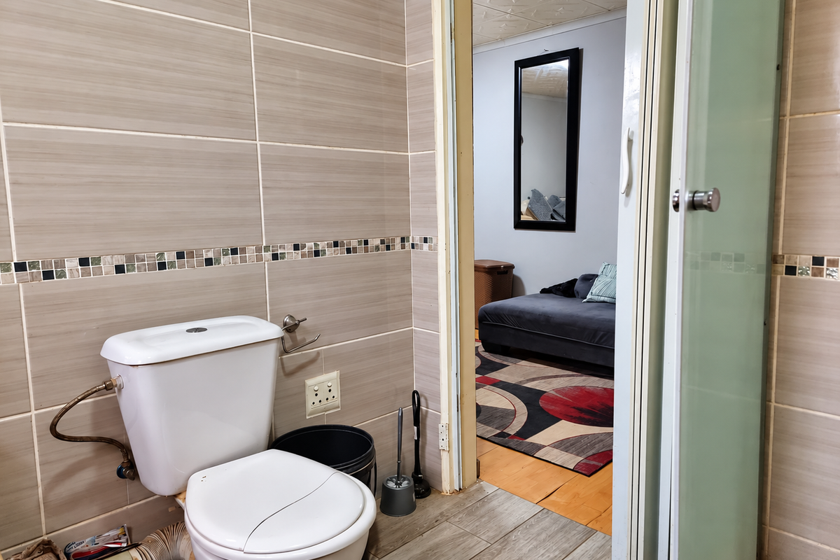 A compact bathroom featuring tiled walls with a mosaic accent, a toilet, and a sliding door leading to an adjacent living space.