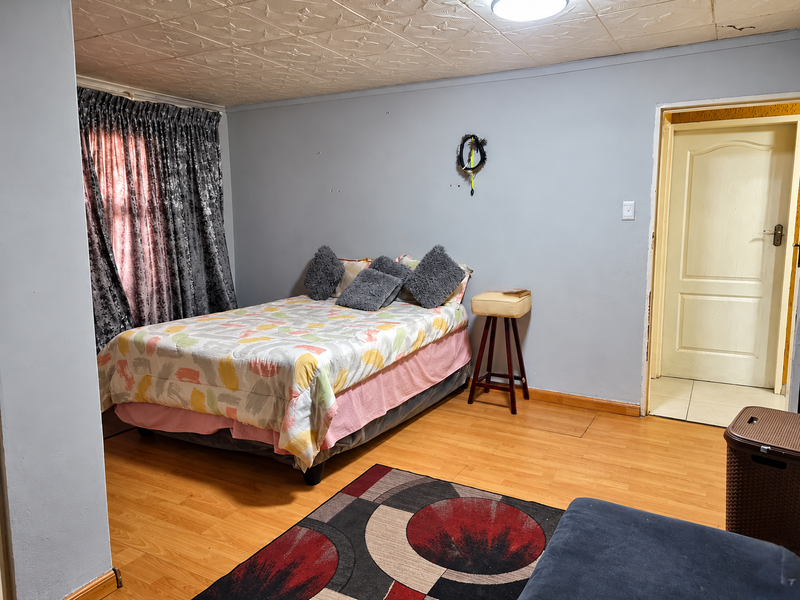 A bedroom featuring laminate flooring and textured ceiling tiles, currently showing signs of wear including ceiling cracks and paint deterioration.