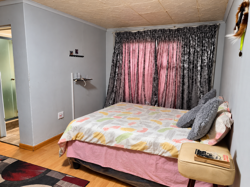 A bedroom featuring laminate flooring, textured ceiling tiles, and direct access to an en-suite bathroom.
