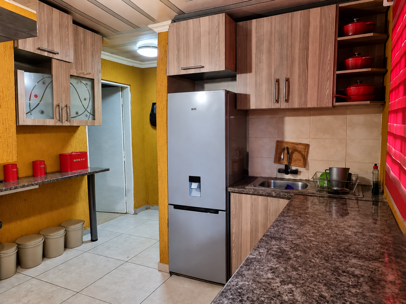 A functional kitchen featuring wood-look laminate cabinetry, granite countertops, a stainless steel sink, and tiled flooring with a bright yellow accent wall.