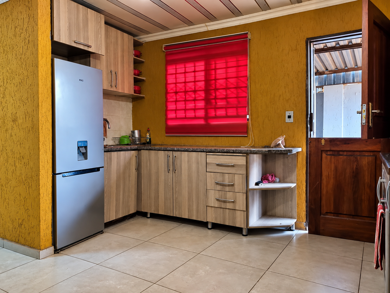 A functional kitchen featuring laminate cabinetry, granite countertops, tiled flooring, and direct access to an outdoor area through a timber door.