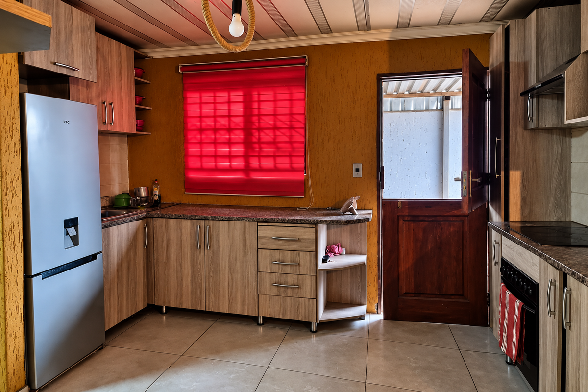 A functional kitchen featuring wood-look cabinetry, granite-style countertops, built-in oven and hob, and a stable door leading to the exterior.