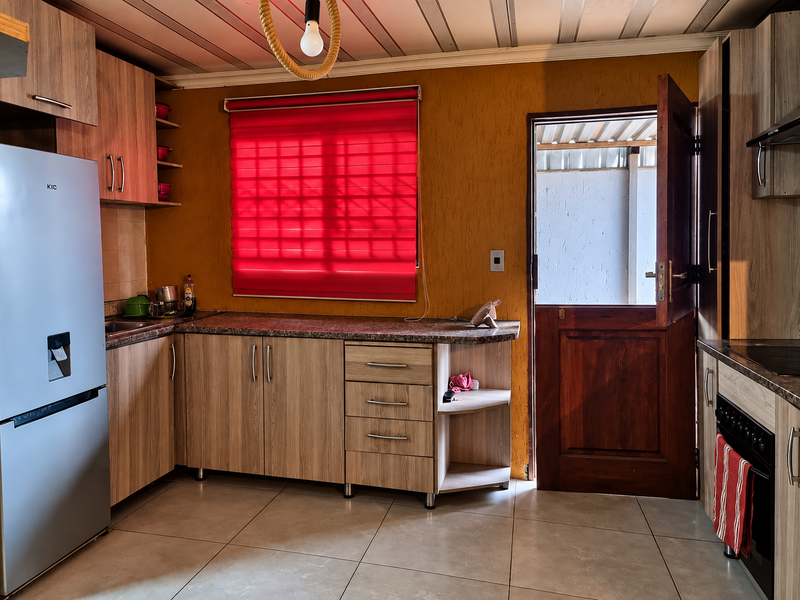 A functional kitchen featuring wood-look cabinetry, granite-style countertops, built-in oven and hob, and a stable door leading to the exterior.
