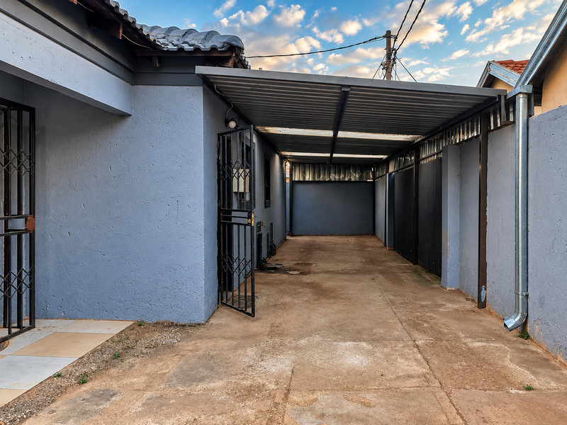 A covered carport area featuring a metal roof structure, concrete paving, and secure gated access to the side of the property.
