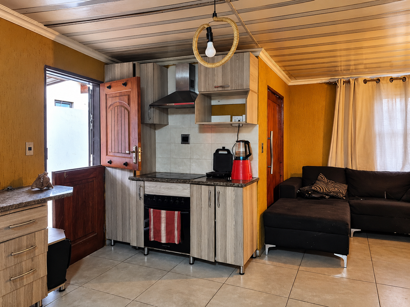 Open-plan living area featuring a compact kitchen with built-in cabinetry, electric hob, oven, and extractor fan, finished with tiled flooring and a stable door.