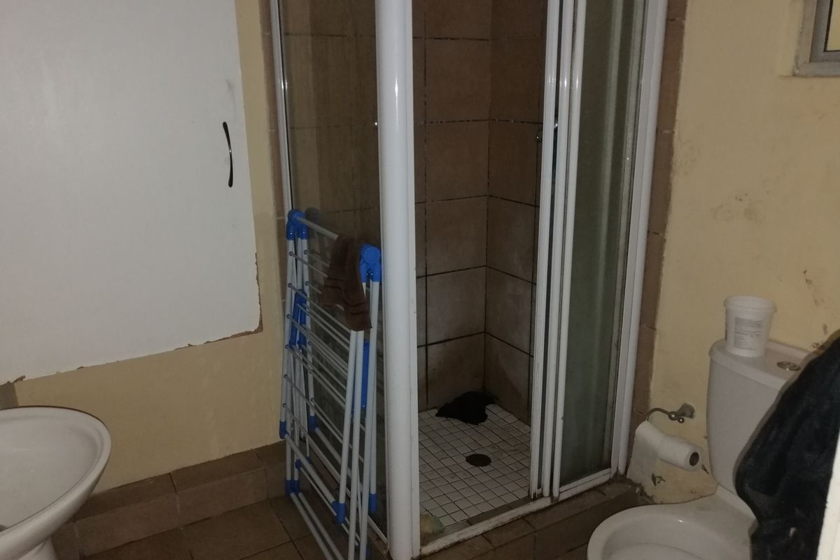 A dated bathroom featuring a shower enclosure, pedestal basin, and toilet, requiring cosmetic updates and maintenance to improve its overall condition.