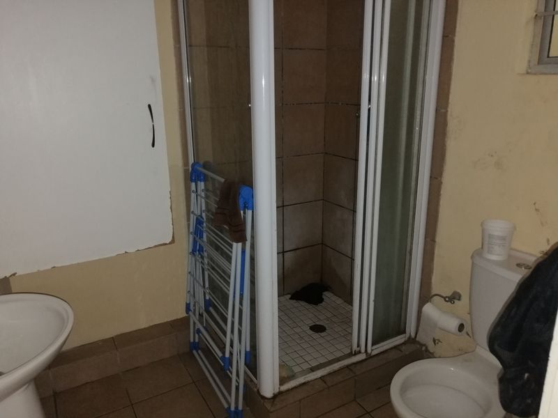 A dated bathroom featuring a shower enclosure, pedestal basin, and toilet, requiring cosmetic updates and maintenance to improve its overall condition.