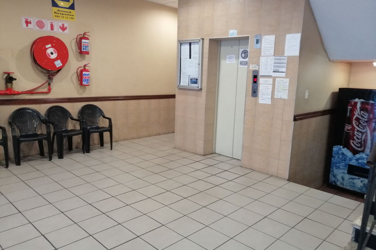 A communal building entrance lobby featuring tiled flooring, wall cladding, an elevator, and essential fire safety equipment.