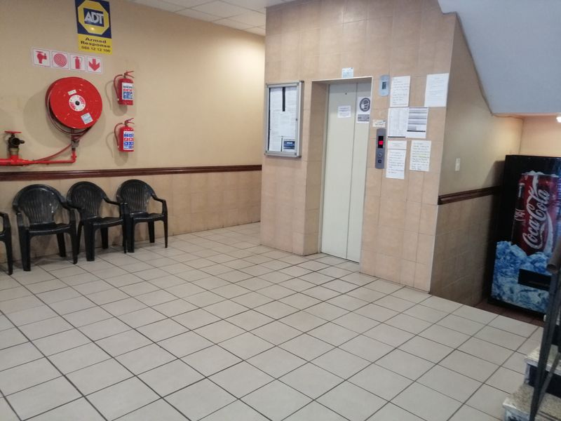 A communal building entrance lobby featuring tiled flooring, wall cladding, an elevator, and essential fire safety equipment.