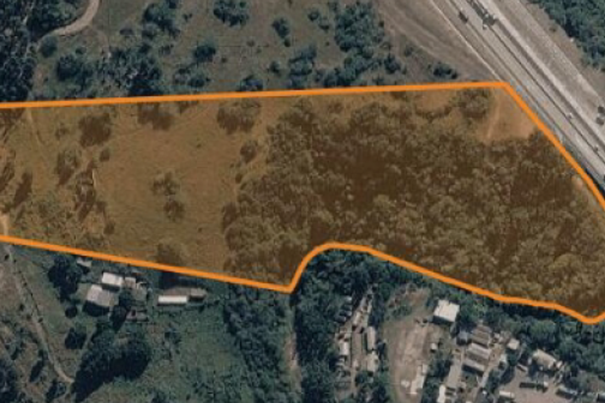 Aerial view of a vacant residential land parcel with natural vegetation and clear boundary markings, situated near a major road.