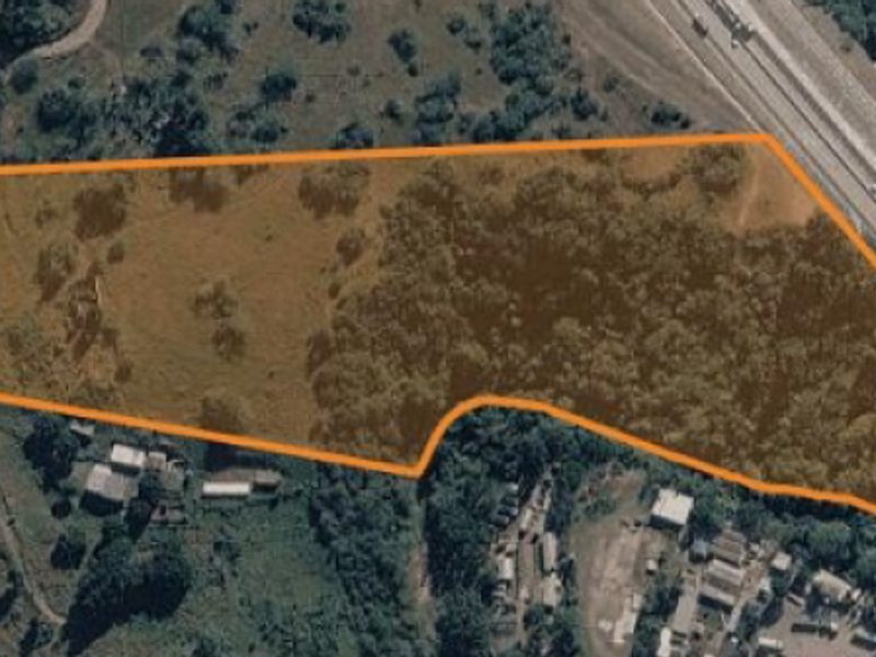 Aerial view of a vacant residential land parcel with natural vegetation and clear boundary markings, situated near a major road.