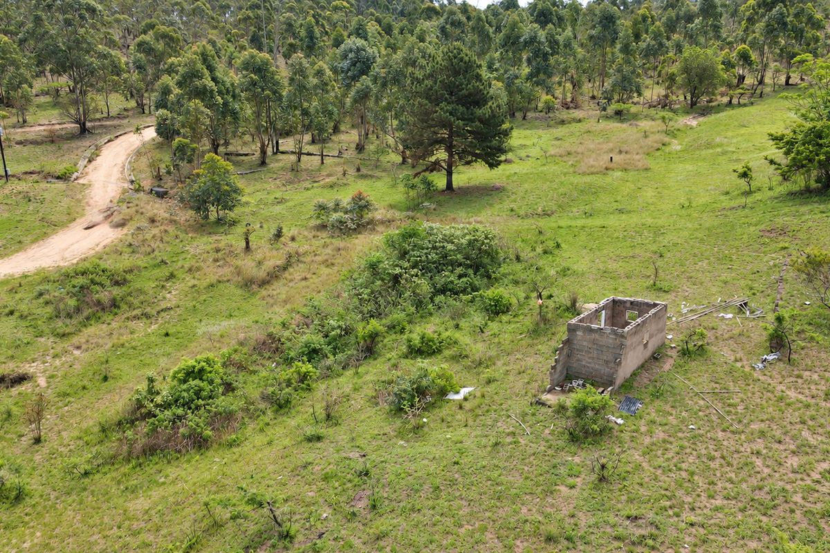 Aerial view of a large vacant residential plot featuring a dirt access road, utility connections, and a small, dilapidated concrete block structure.