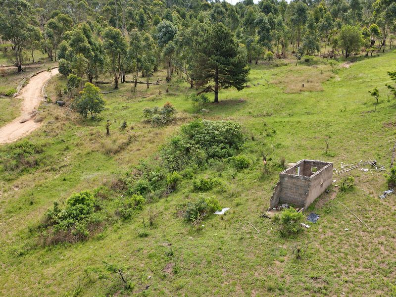 Aerial view of a large vacant residential plot featuring a dirt access road, utility connections, and a small, dilapidated concrete block structure.