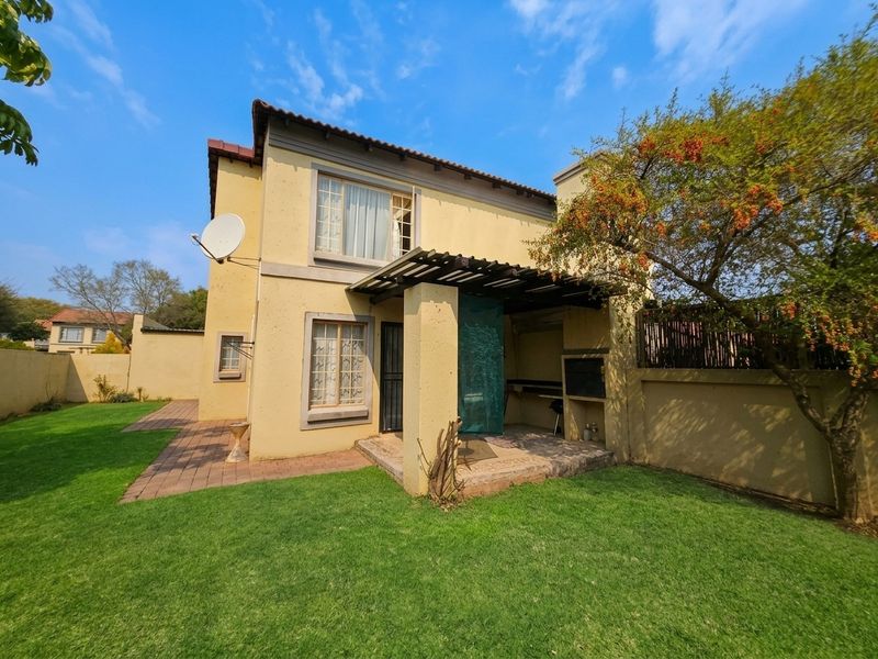 Rear view of the townhouse featuring a paved patio with a built-in braai, pergola, and a private garden area.