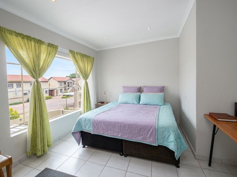 A bright and well-maintained bedroom featuring tiled flooring, recessed ceiling lights, and a large window offering a view of the surrounding townhouse complex.