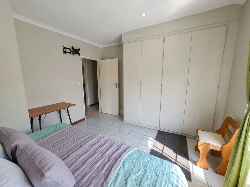 A bedroom featuring tiled flooring, built-in cupboards, and a wall-mounted TV bracket, offering a functional and neutral living space.