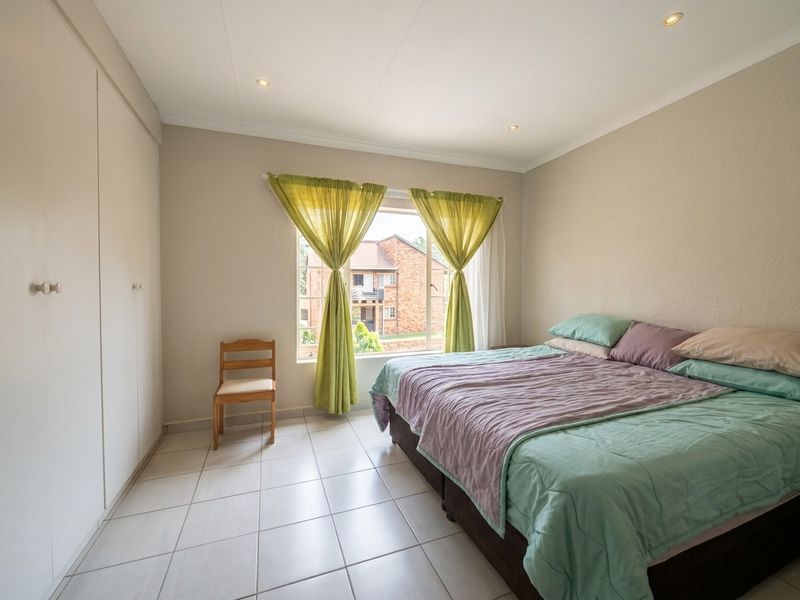 A well-lit bedroom featuring neutral walls, tiled flooring, recessed ceiling lights, and ample built-in cupboard storage space.