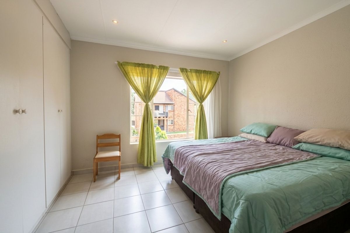 A well-lit bedroom featuring neutral walls, tiled flooring, recessed ceiling lights, and ample built-in cupboard storage space.