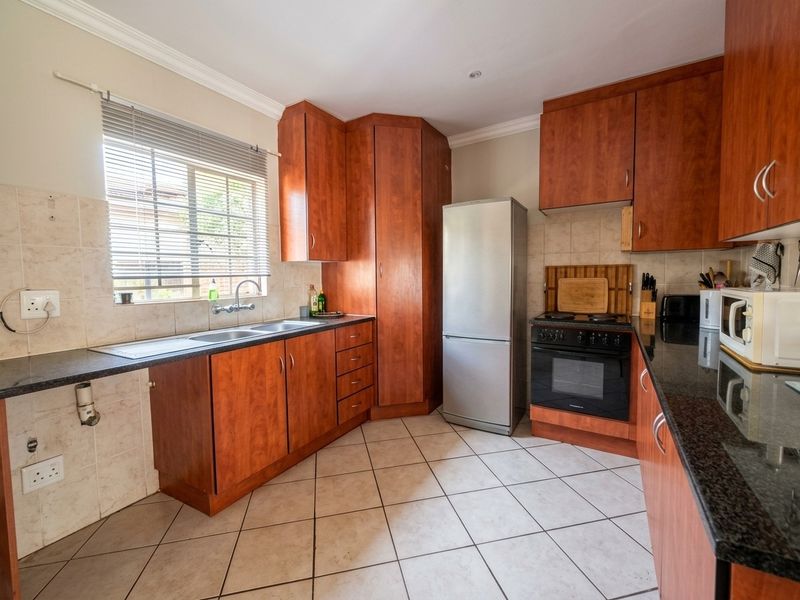 A functional kitchen featuring cherry wood cabinetry, granite countertops, tiled flooring, and a double basin sink with a tiled splashback.
