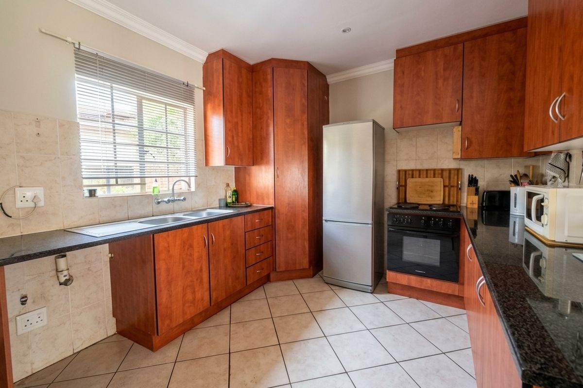 A functional kitchen featuring cherry wood cabinetry, granite countertops, tiled flooring, and a double basin sink with a tiled splashback.