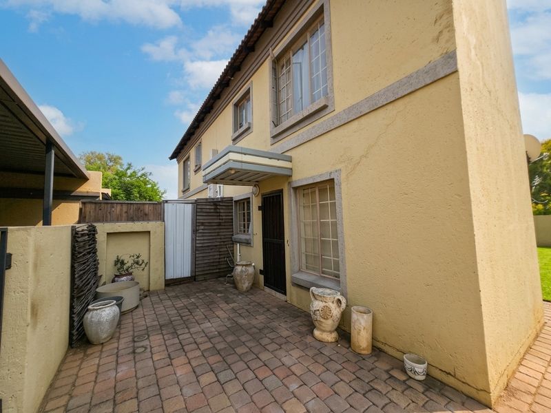 Rear exterior view of the townhouse featuring a paved patio area, security gate, and traditional plaster finish with tiled roof.