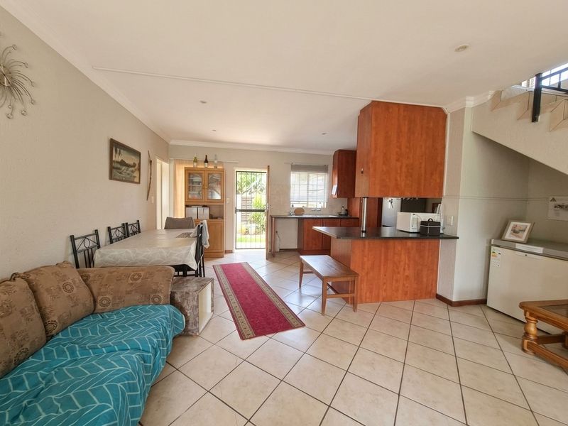 Open-plan living and dining area featuring tiled flooring, a functional kitchen with built-in cabinetry, and direct access to the rear exterior.