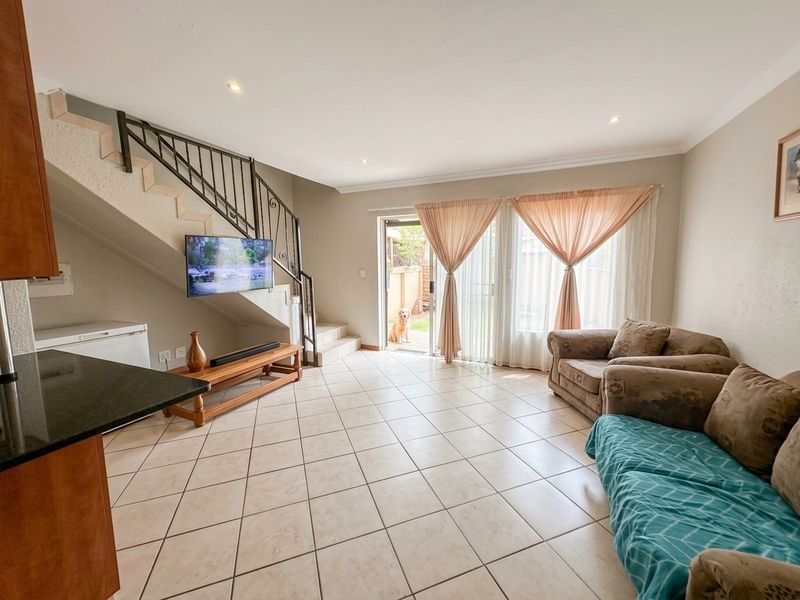 Open-plan living area featuring tiled flooring, a staircase with metal balustrades, and sliding glass doors providing access to the rear patio.