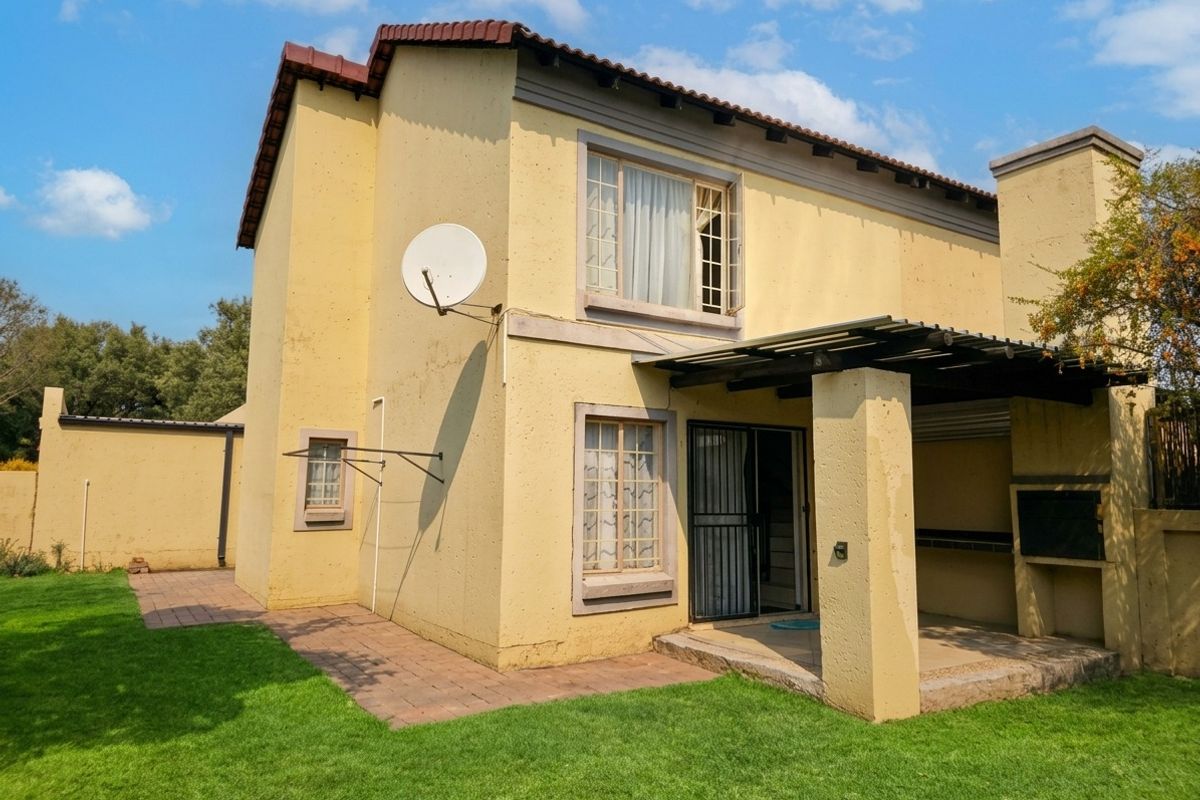 Rear view of the townhouse featuring a covered patio with a built-in braai, paved walkway, and a private garden area.