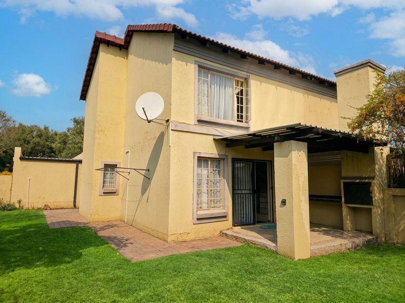 Rear view of the townhouse featuring a covered patio with a built-in braai, paved walkway, and a private garden area.
