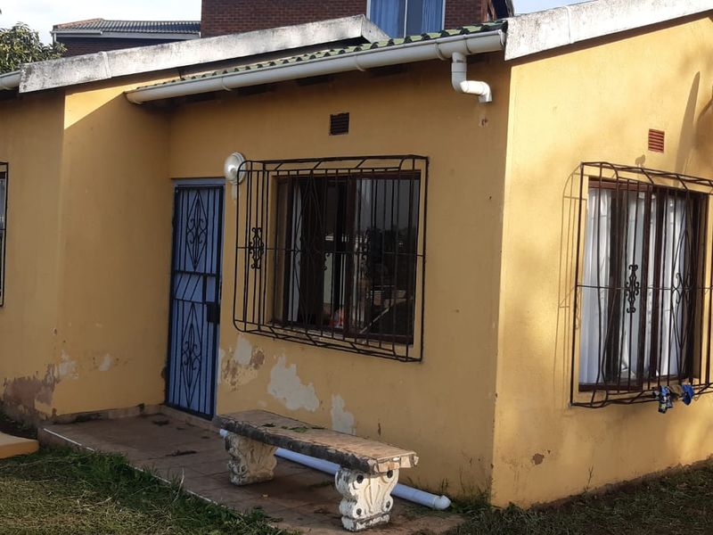 Exterior view of a single-story house featuring yellow painted walls, security bars on windows, and a tiled entrance area.
