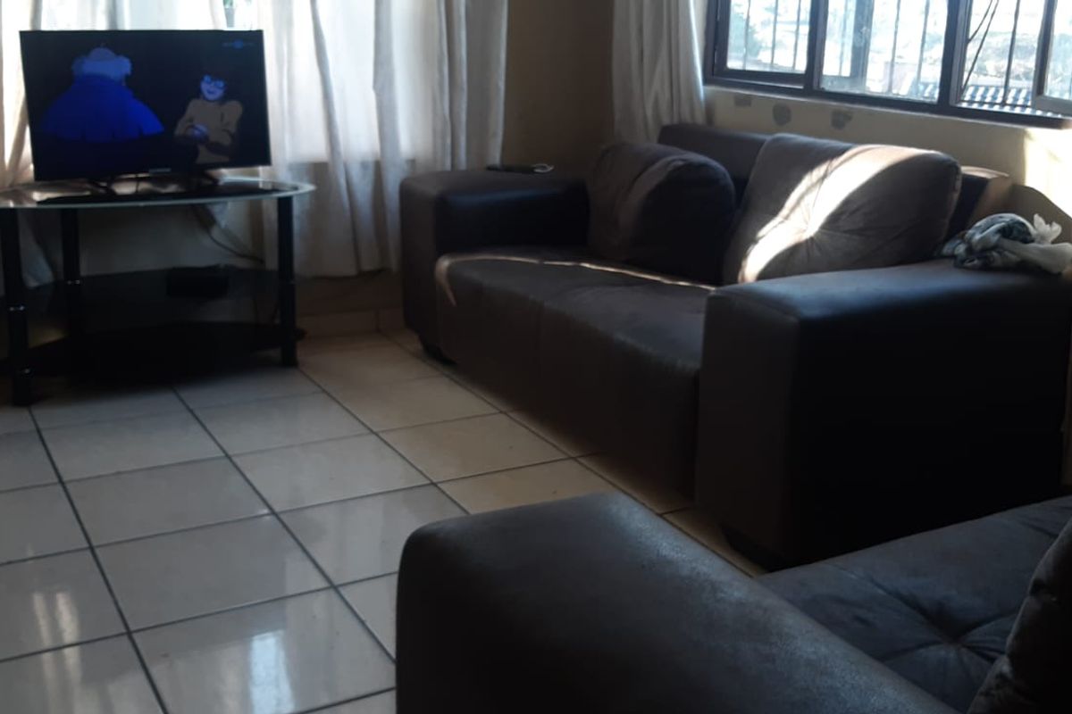 A living room featuring tiled flooring and a window with security bars, requiring minor cosmetic updates to the wall finishes.