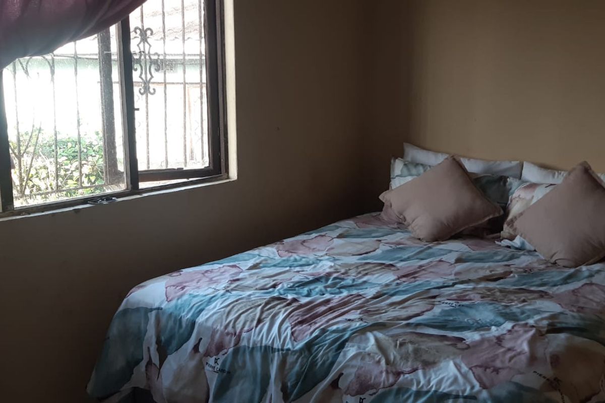 A bedroom featuring a window with security bars and plain wall finishes, requiring cosmetic updates to improve the overall aesthetic.