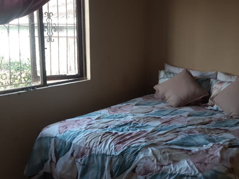 A bedroom featuring a window with security bars and plain wall finishes, requiring cosmetic updates to improve the overall aesthetic.