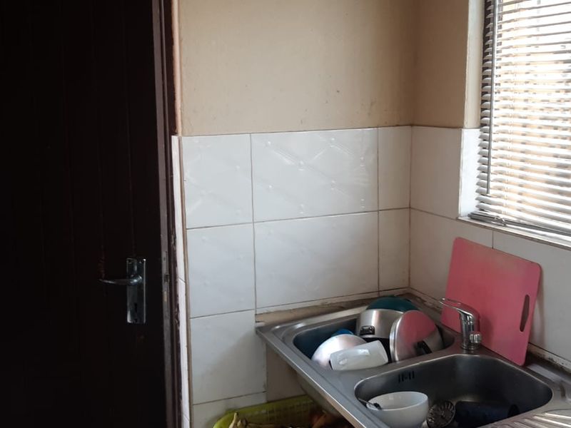 A compact scullery area featuring a stainless steel double sink, tiled splashback, and natural light through a window with venetian blinds.